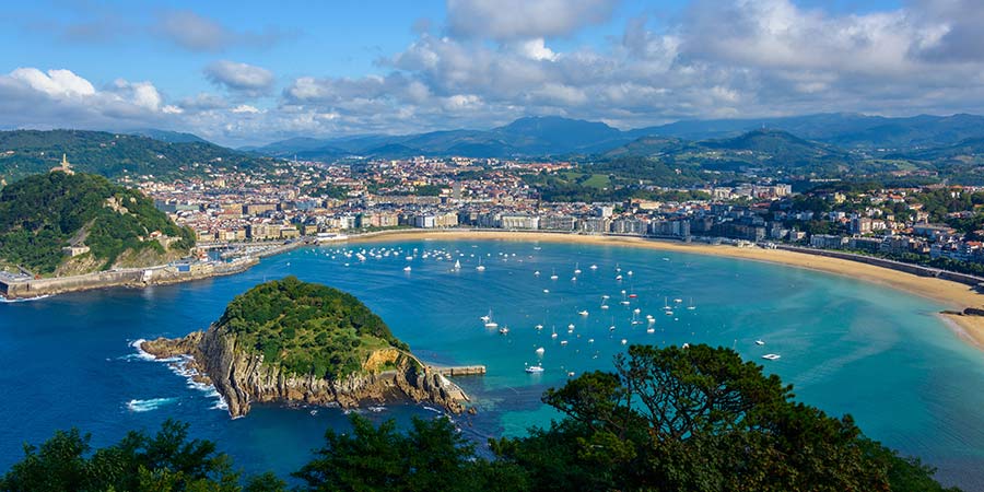 The beautiful bay of San Sebastián features bright blue water, pale yellow sand and many boats sailing on the water. 